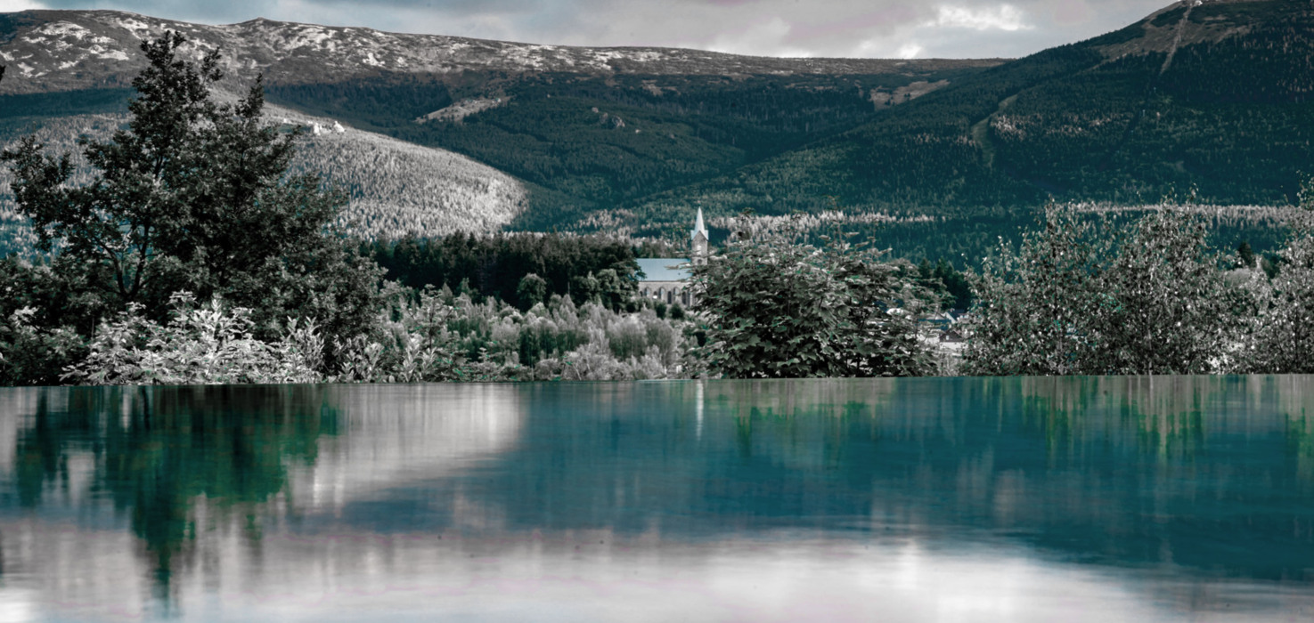 Infinity-Pool mit Blick auf Berglandschaft und eine Kirche umgeben von Bäumen