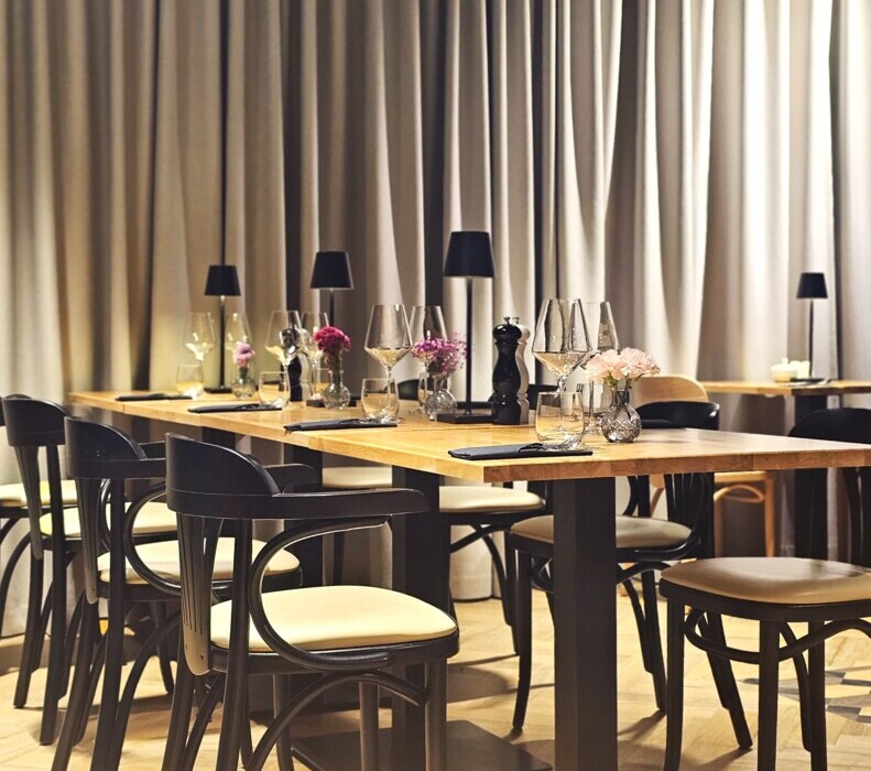 Elegancka restauracja z drewnianymi stołami, czarnymi krzesłami i delikatnym oświetleniem przy świeżych kwiatach na stołach.