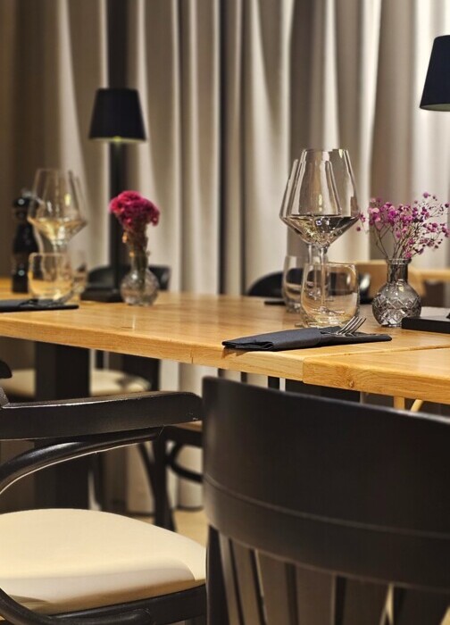 Elegancki drewniany stół z czarnymi krzesłami, kieliszkami i drobnymi wazonikami z kwiatami w nowoczesnej restauracji