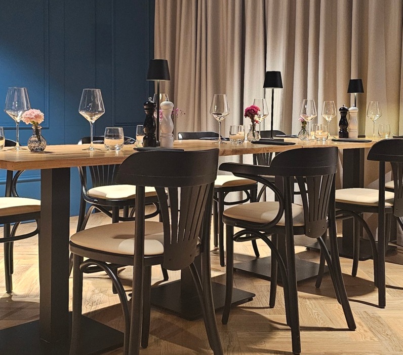 Nowoczesna restauracja z drewnianym stołem, czarnymi krzesłami i eleganckim oświetleniem, stworzona na kameralne kolacje