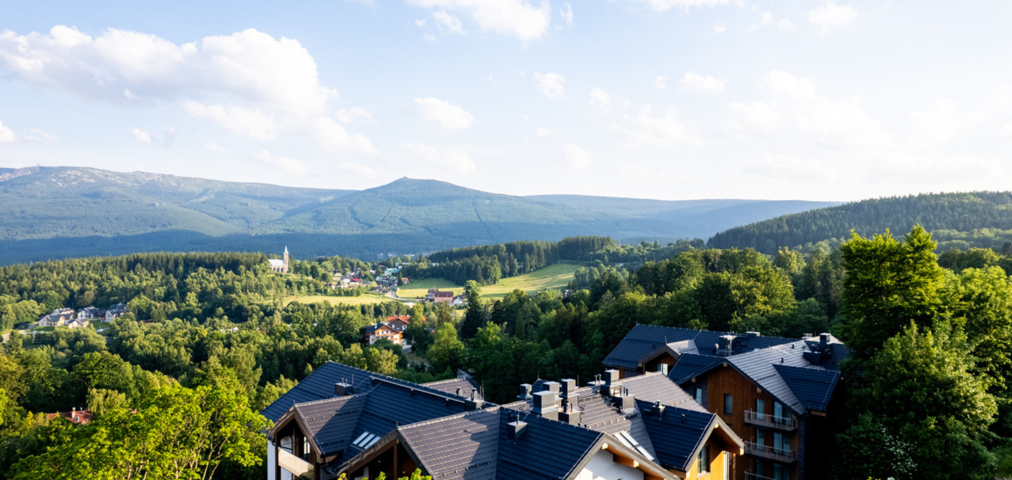 Nowoczesny hotel z widokiem na zielone wzgórza i lasy, otoczony naturą w górskiej okolicy.