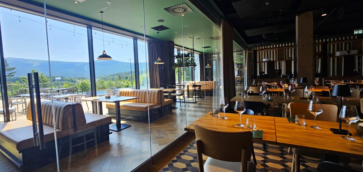 Restauracja z nowoczesnym drewnianym wystrojem, wygodne kanapy i stoliki przy dużych oknach z widokiem na góry.