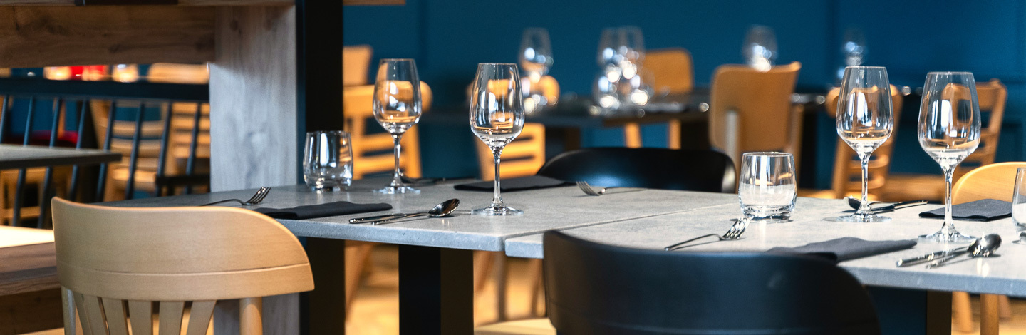 Elegancko przygotowany stół w restauracji hotelowej z kieliszkami i sztućcami na szarym blacie.