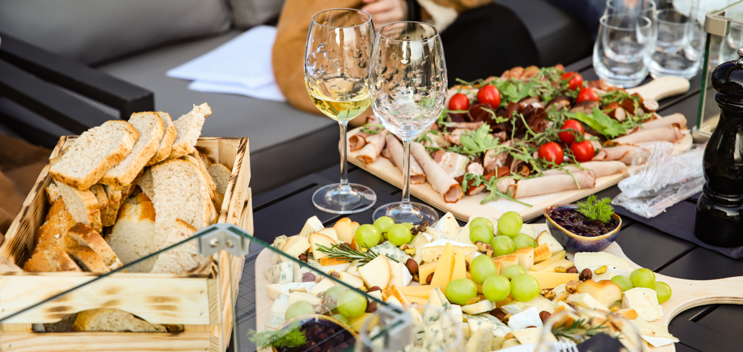 Deska serów z winogronami, wędlinami i świeżym pieczywem serwowana przy eleganckim stole na zewnątrz z kieliszkami wina.