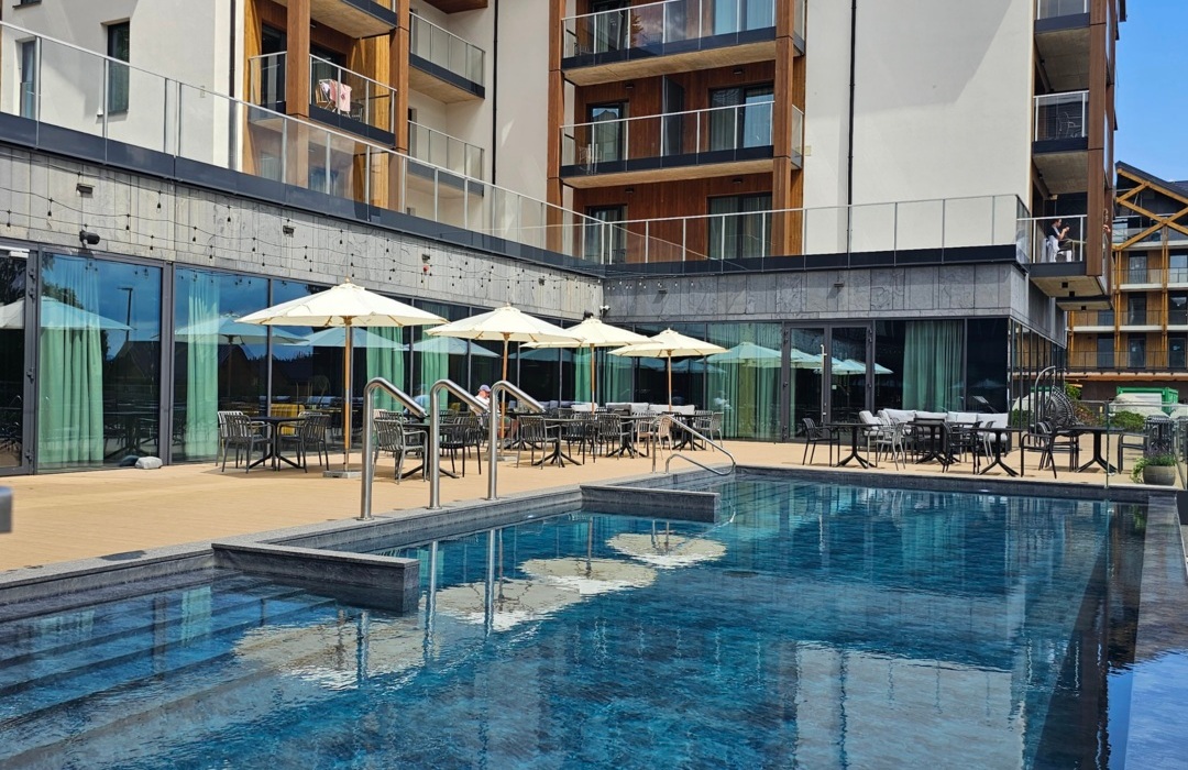 Nowoczesny hotel z basenem na świeżym powietrzu, tarasem z leżakami i parasolami oraz drewnianymi balkonami pokojów