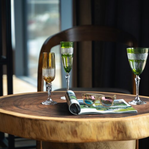 Eleganter Tisch aus Naturholz mit drei Kristallgläsern, Magazin und Sonnenbrille in modernem Hotelambiente