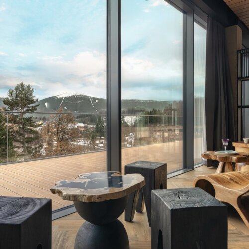 Moderne Hotelterrasse mit Holzmöbeln und Panoramablick auf verschneite Berge und Waldlandschaft.