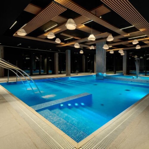 Luxuriöser Innenpool im Hotel mit LED-Beleuchtung, Wasserfontänen und modernem Holzdecken-Design.