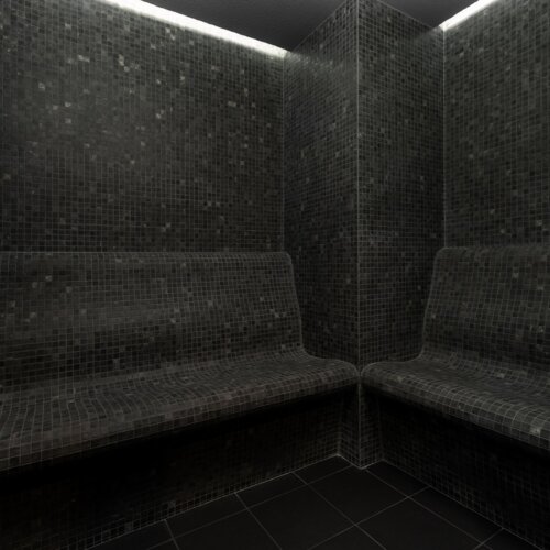 Dunkle Dampfbad-Sauna mit gefliesten Bänken und Wänden für eine entspannende Spa-Atmosphäre.