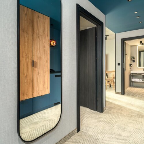 Geräumiger Hotelflur mit großem Spiegel, Holzschränken und Blick ins Bad und Essbereich.