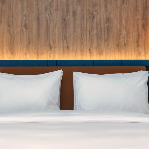 Hotelbett mit weißer Bettwäsche, dunkelblauem Kopfteil und modernen roten Hängelampen an beiden Seiten