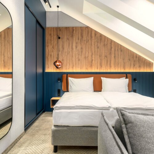 Modernes Hotelzimmer im Dachgeschoss mit Doppelbett, Holzvertäfelter Wand und dezenter LED-Beleuchtung
