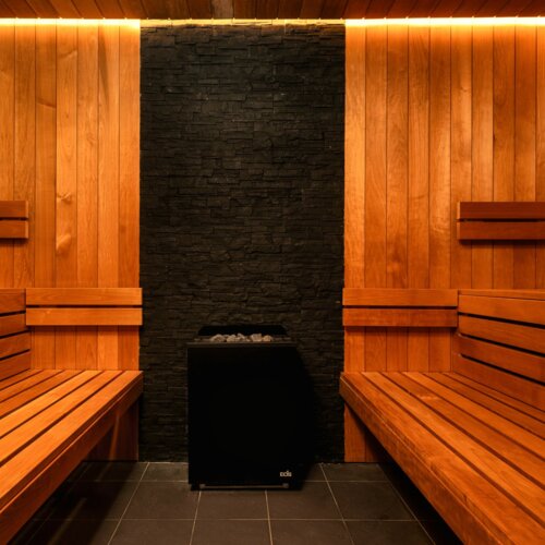 Moderne Sauna mit Holzbanken und schwarzer Steinwand, beheizt durch einen elektrischen Ofen