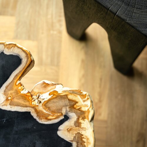 Nahaufnahme eines luxuriösen Holztisches mit natürlicher Kante und schwarzem Sockel auf hellem Holzboden