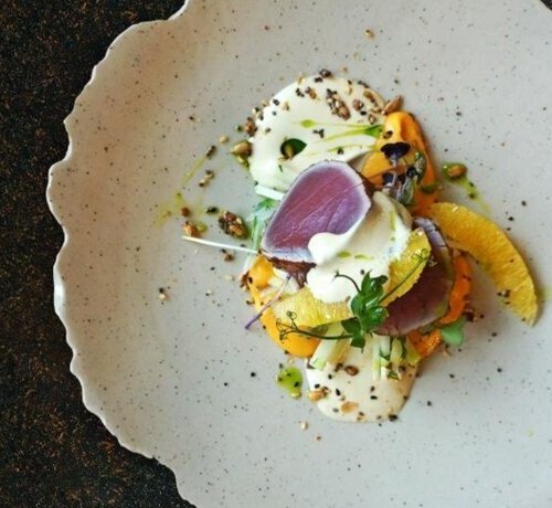 Elegante Vorspeise mit rohem Thunfisch, Orangenscheiben, cremiger Soße und Samen auf dekorativem Teller