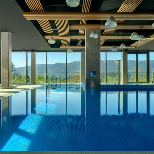 Großer Innenpool im Hotel mit bodentiefen Fenstern und Bergblick, ausgestattet mit Liegestühlen zum Entspannen.