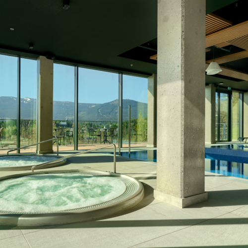 Modernes Spa mit zwei runden Whirlpools und Schwimmbad, große Fenster mit Bergblick und Terrasse mit Sitzgelegenheiten