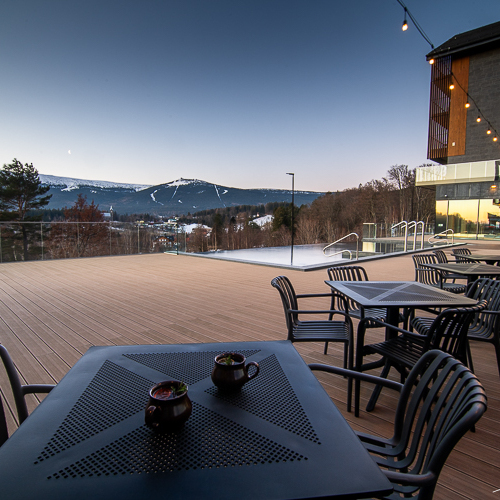 Großzügige Hotelterrasse mit Metalltischen und Stühlen, Bergblick in der Dämmerung, stimmungsvolle Lichterkette
