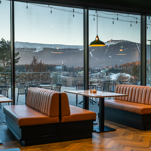 Restaurant mit bequemen Lederbänken und großen Fenstern mit Blick auf Berglandschaften bei Sonnenuntergang