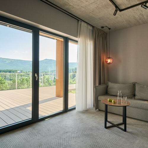 Modernes Zimmer mit grauem Sofa, runden Tisch und großem Balkon mit Blick auf grüne Berge
