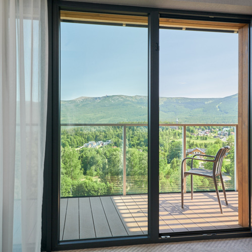 Hotelbalkon mit Metallstuhl und Panoramablick auf grüne Hügel und Dorf unter dem Berg