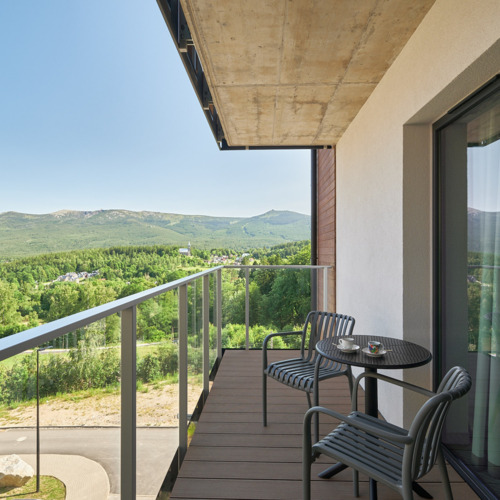 Balkon mit zwei Stühlen und Tisch mit Tassen, Blick auf grüne Hügel und bewaldete Berge.