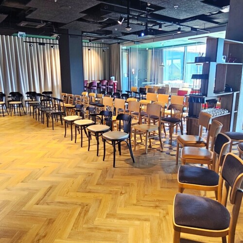 Moderne Konferenzraum mit Holzstühlen, die auf eine große Projektionsfläche ausgerichtet sind, natürliches Licht durch bodentiefe Fenster