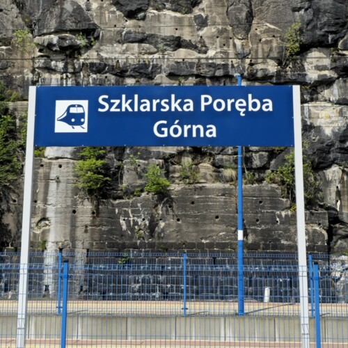 Bahnhof Szklarska Poręba Górna mit blauem Schild vor felsiger Klippe und grünem Bewuchs