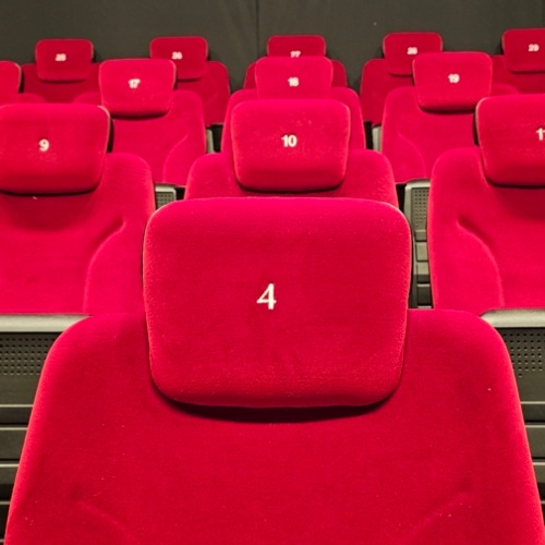 Bequeme, nummerierte rote Samtsitze in einem gemütlichen Kinosaal mit gedämpfter Beleuchtung und dunklen Wänden.