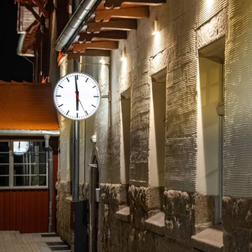 Ruhige Hotelfassade bei Nacht mit Steinmauerwerk, warmer Beleuchtung und großer Uhr an der Wand