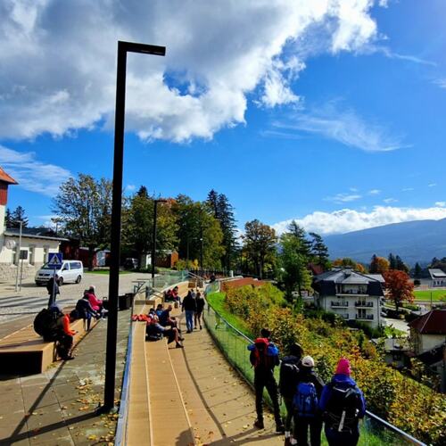Traditionelles Gebäude mit rotem Ziegeldach und Touristen, die auf einem Weg mit Blick auf die Berge spazieren