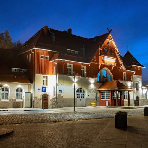 Charmantes Hotelgebäude bei Nachtbeleuchtung mit traditioneller Architektur, roter Holzfassade und steinerner Basis in ruhiger Straße