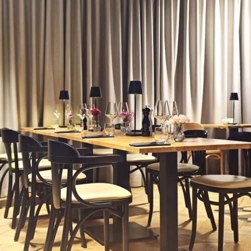 Elegantes Restaurant mit Holztischen, schwarzen Stühlen, sanfter Beleuchtung und frischen Blumen in Vasen auf den Tischen.