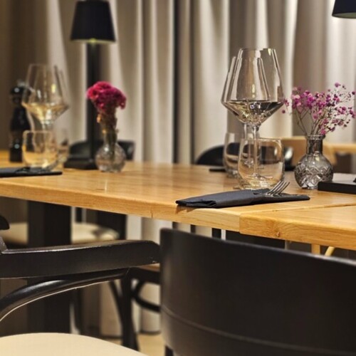 Eleganter Holztisch mit schwarzen Stühlen, Weingläsern und kleinen Blumenväschen in modernem Restaurant