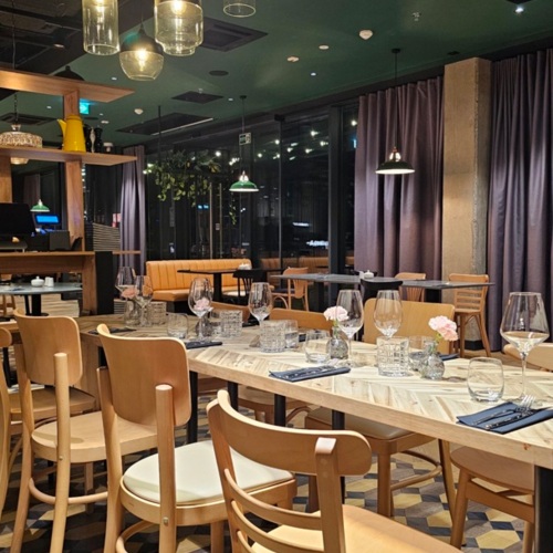 Modernes Restaurant mit Holzstühlen, elegant gedeckten Tischen und warmem Pendellicht für gemütliche Stimmung