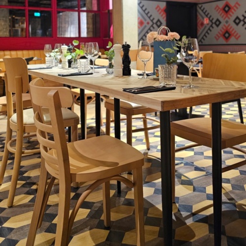 Eleganter Hoteltisch mit Holzstühlen, Blumenarrangements und Glasgeschirr in modernem Raum mit geometrischem Bodenmuster.