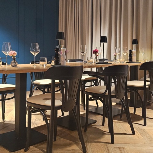 Modernes Restaurant mit Holztisch, schwarzen Stühlen und stilvoller Beleuchtung, ideal für gemütliche Abendessen