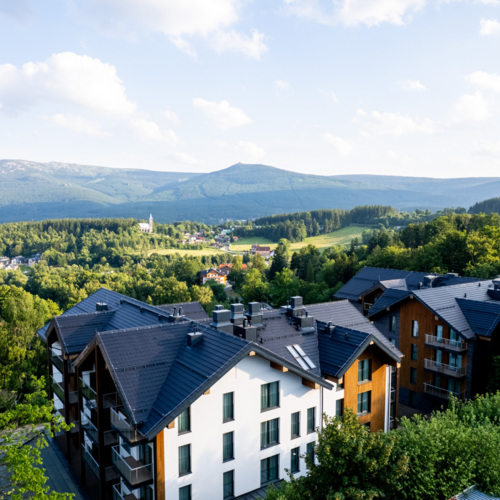 Hotel mit modernen Zimmern und Balkonen, umgeben von grünen Wäldern mit Blick auf das Bergpanorama
