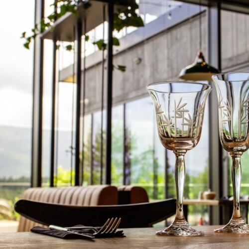 Elegante Kristallgläser auf einem Tisch in einem Restaurant mit Bergblick durch große Bodenglasfenster.