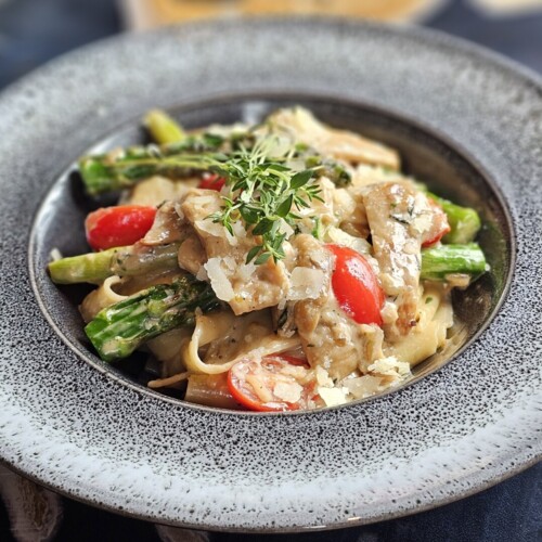 Nudeln mit Hähnchen, Spargel, Cherrytomaten und Parmesan, serviert auf einem stilvollen Teller im Hotelrestaurant