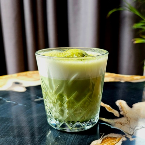 Glas mit grünem Matcha-Getränk und Schaum auf elegantem Marmortisch im Hotelrestaurant