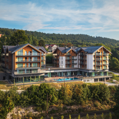 Modernes Hotel im Wald mit großen Balkonen und Außenpool, umgeben von grünen Hügeln und Bäumen
