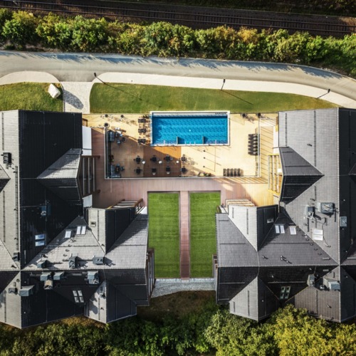 Luxushotel mit dunklen Satteldächern, großem Außenpool, Liegestühlen und großzügiger Terrasse im Grünen