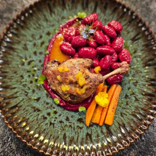 Gewürzte Entenkeule mit Fruchtsauce, rosa Gnocchi und gerösteten Karotten auf dekorativem Teller