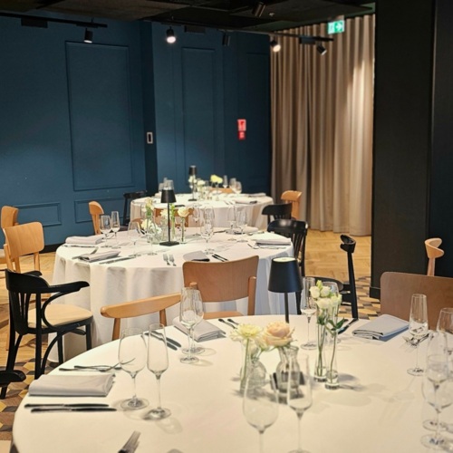 Eleganter Speiseraum mit runden Tischen, weißen Tischdecken, Blumenarrangements und stilvoller Beleuchtung.