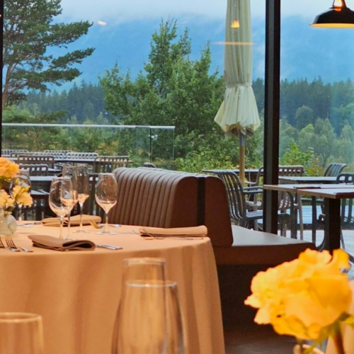 Elegantes Restaurant mit gedeckten Tischen und Terrasse mit Blick auf bewaldete Berge und grünes Laub