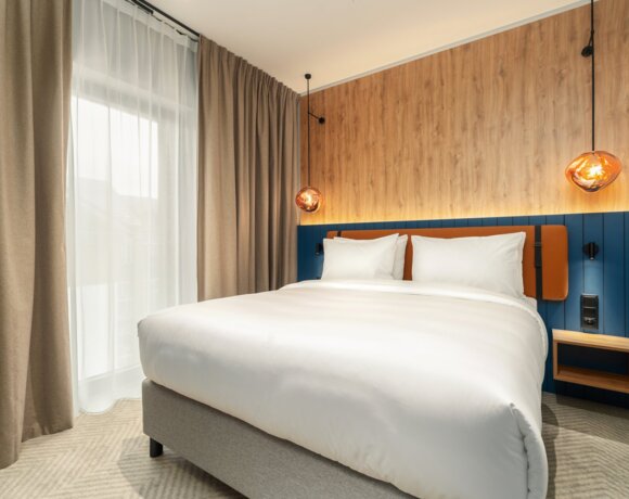 Modern hotel room with king-size bed, wooden accent wall, blue panel, and warm copper pendant lights