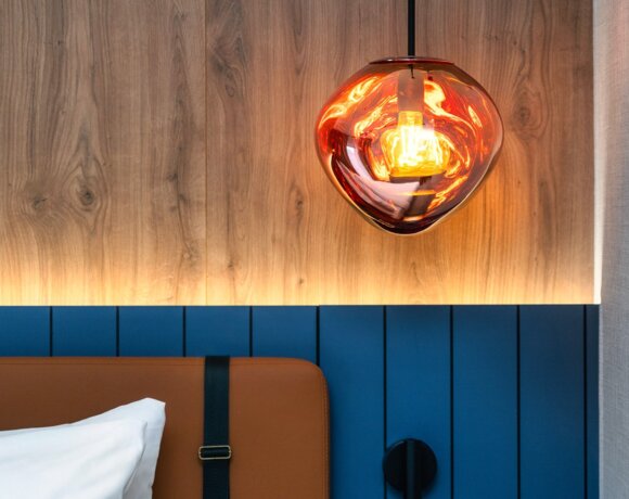 Warme hängende Lampe über Leder-Kopfteil mit blauen Paneelen und Holzverkleidung an der Wand