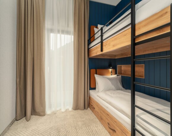 Cozy room with wooden bunk beds, soft curtains, and blue paneled wall, perfect for families and groups.