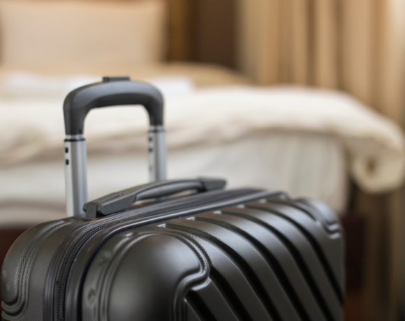 Suitcase with telescopic handle in front of a cozy, bright hotel room bed with neatly arranged bedding